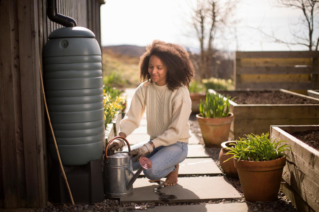 Vrouw bij een regenton in de tuin